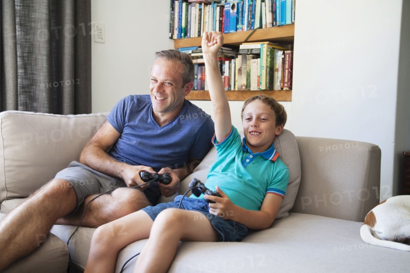 Caucasian father and son playing video games on sofa