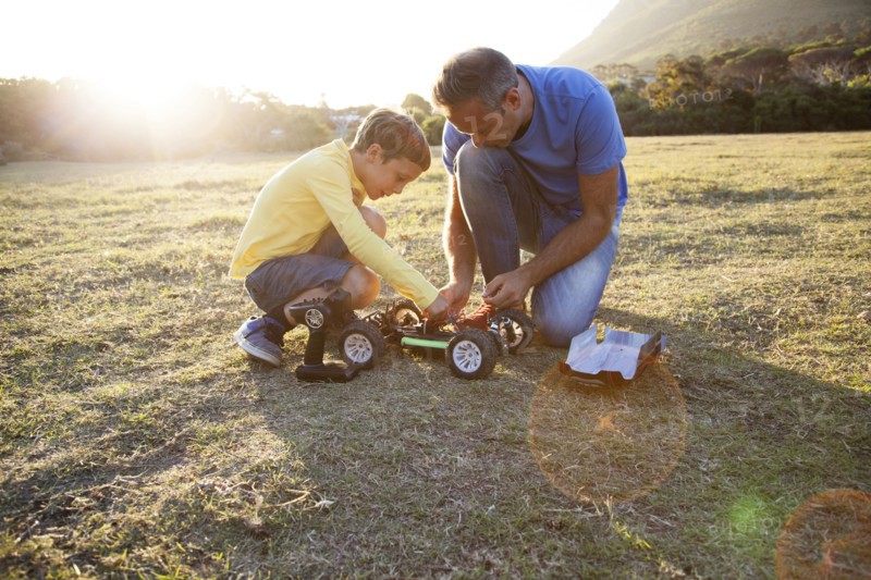 Caucasian father and son playing with remote control cars in field