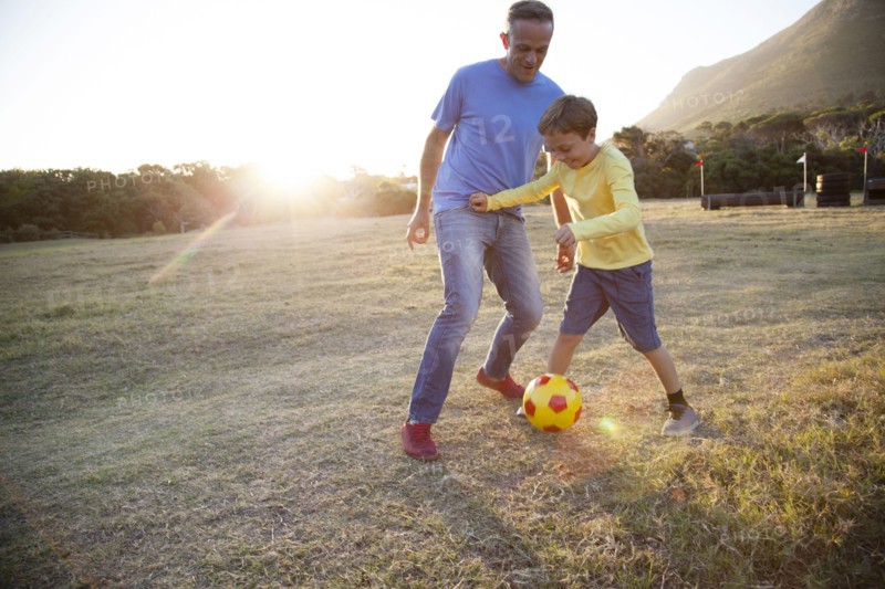 Caucasian father and son playing soccer in field