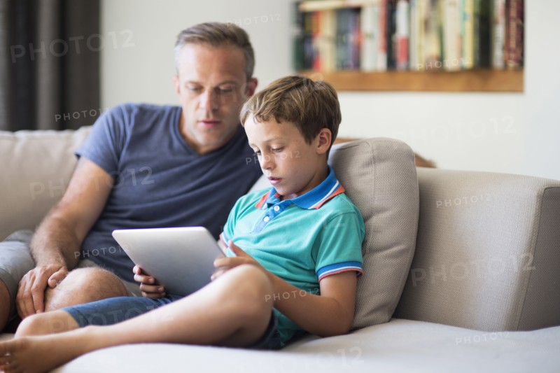 Caucasian father and son using digital tablet on sofa