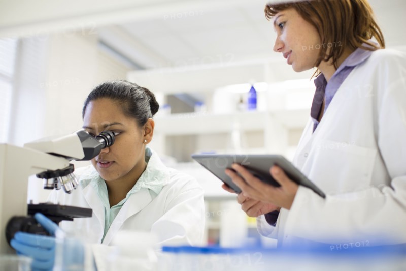 Scientists using digital tablet and microscope in laboratory