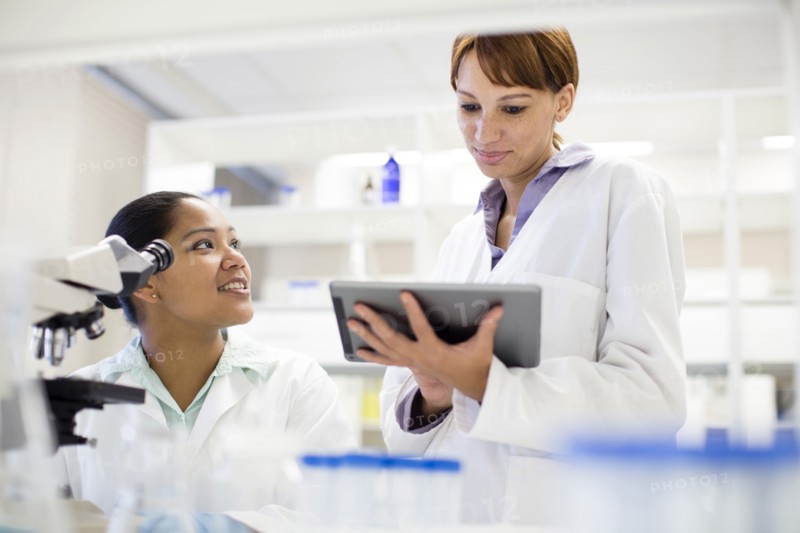 Scientists using digital tablet and microscope in laboratory