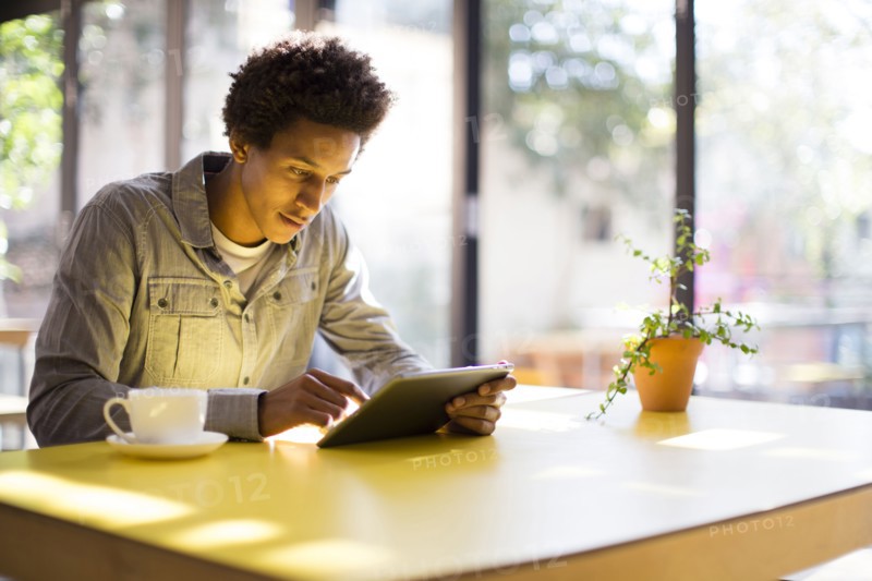 Mixed race man using digital tablet in cafe