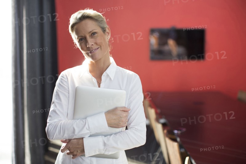 Caucasian businesswoman carrying laptop in conference room