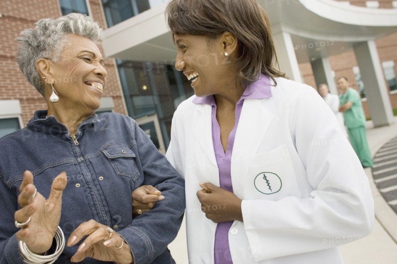 African female doctor laughing with senior African woman outdoors