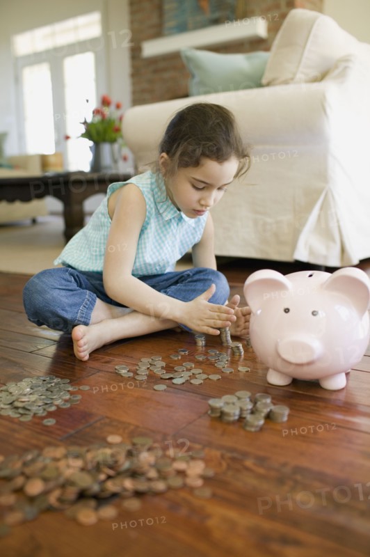 Young girl counting money next to piggy bank