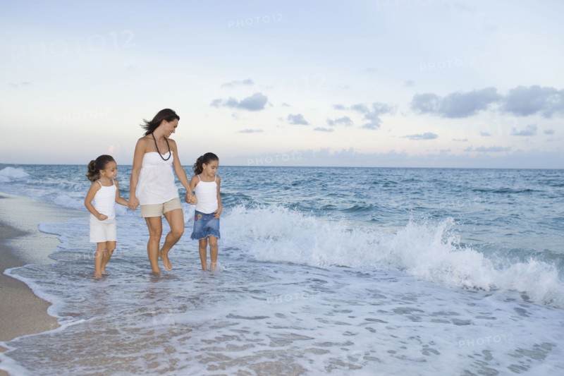 Multi-ethnic mother and daughters walking through ocean surf