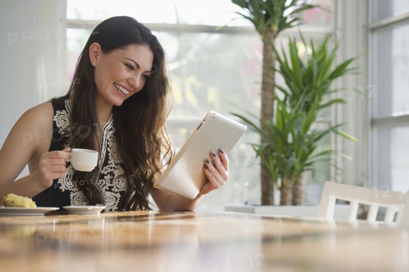 Hispanic woman drinking coffee and using digital tablet