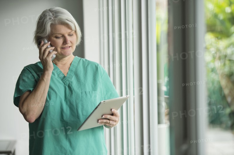 Caucasian surgeon in scrubs using cell phone and digital tablet