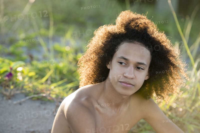 Mixed race teenage boy sitting on beach