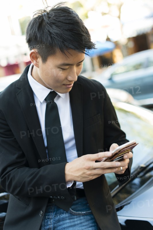 Korean businessman using cell phone near car