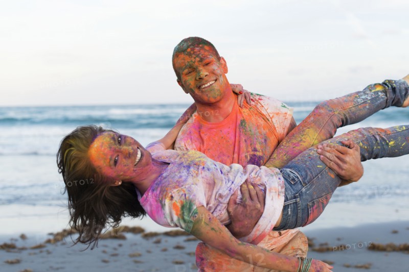 Caucasian couple splattered with paint powder on beach