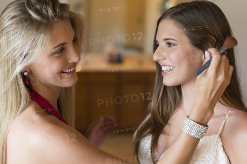 Caucasian bridesmaid applying makeup on bride
