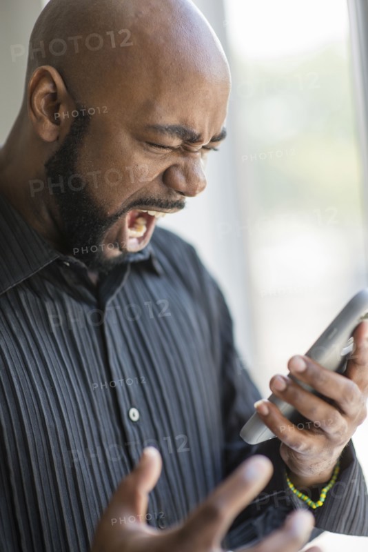 Frustrated black man using cell phone near window