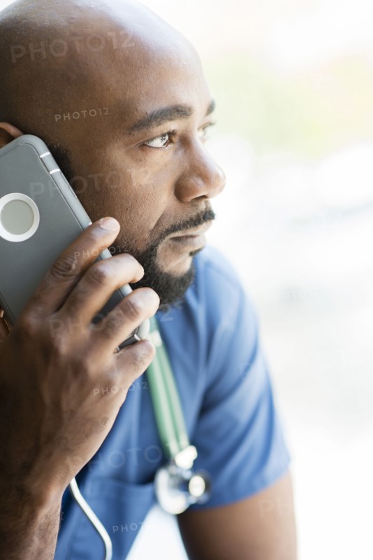 Black nurse talking on cell phone near window