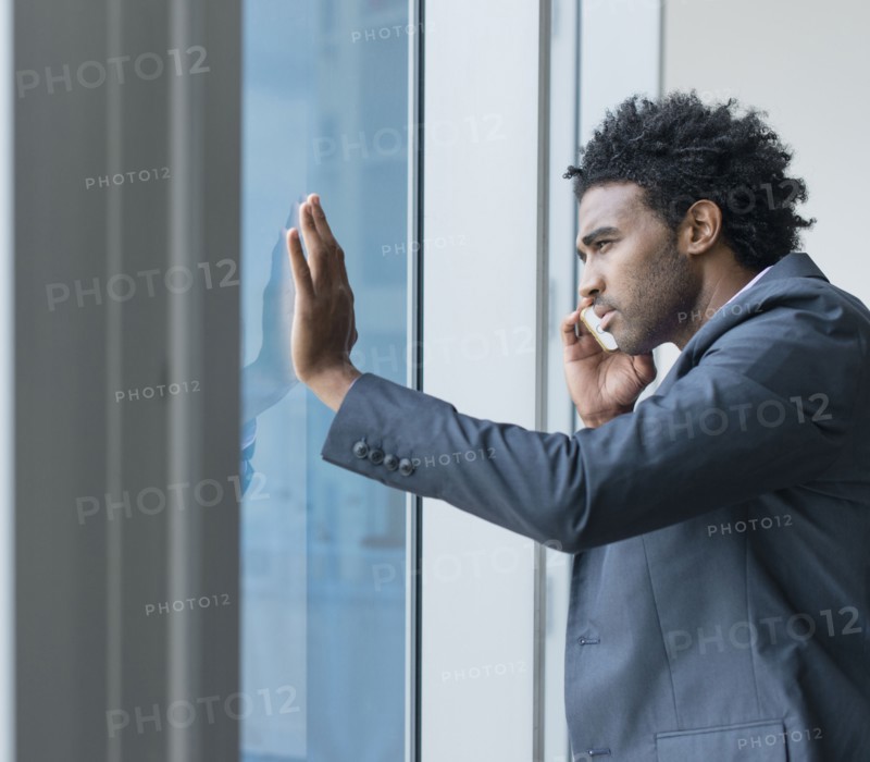 Hispanic businessman talking on cell phone at office window