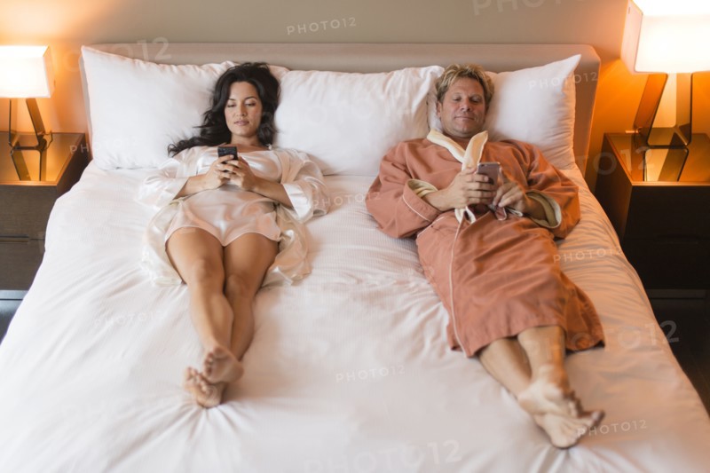 Couple using cell phones on bed