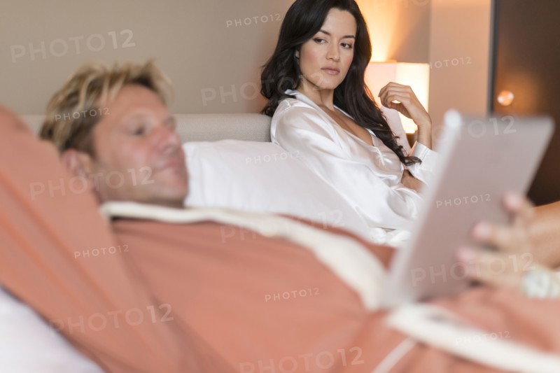 Man with digital tablet ignoring girlfriend in bed