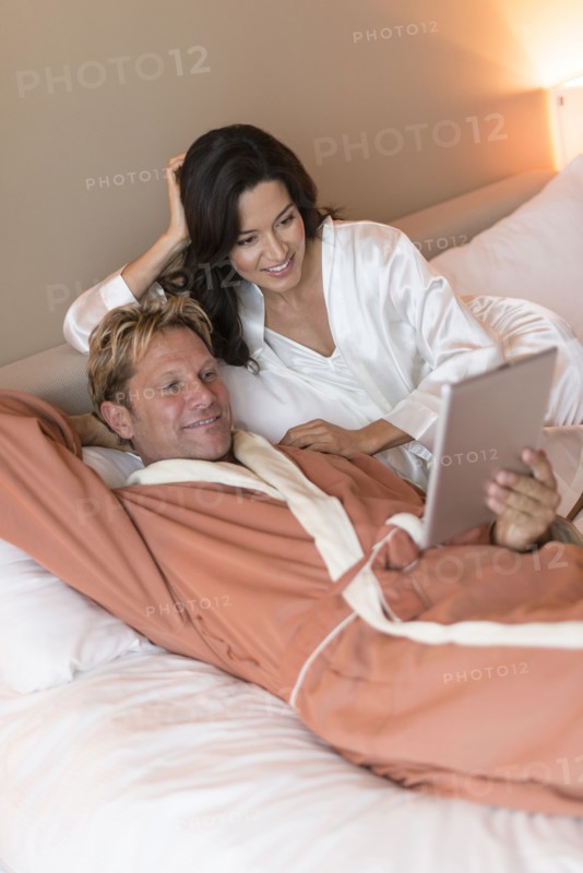 Couple using digital tablet on bed