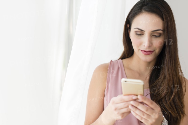 Businesswoman using cell phone near curtain