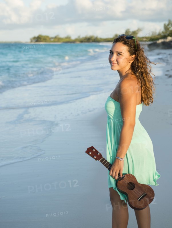 Hispanic teenage girl holding ukulele on beach