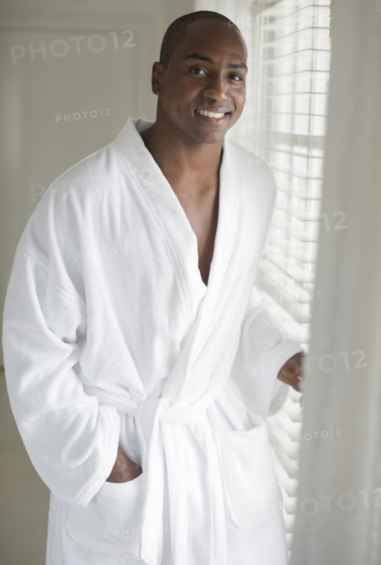 Black man in bathrobe standing at window