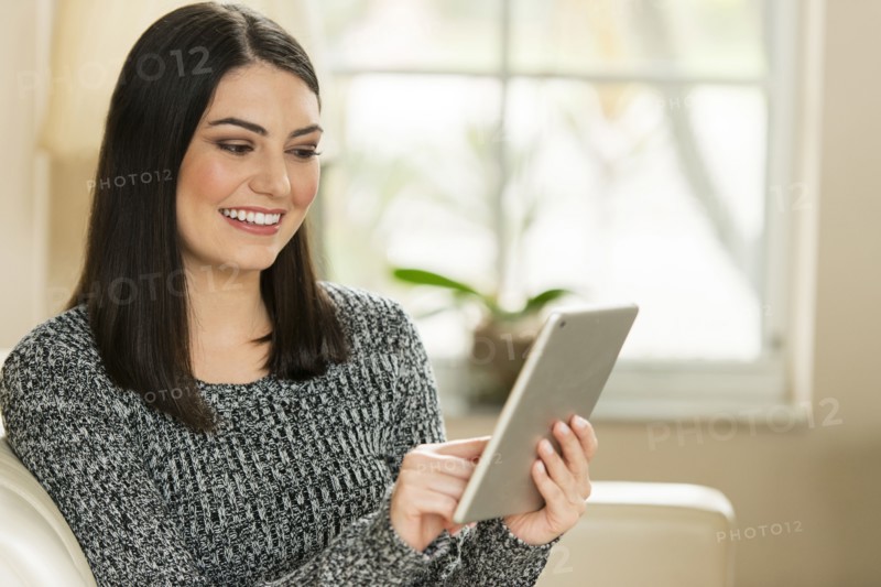 Hispanic woman using digital tablet on sofa