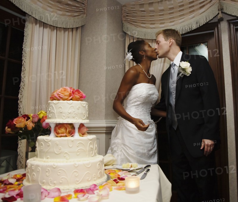Bride and groom kissing next to wedding cake