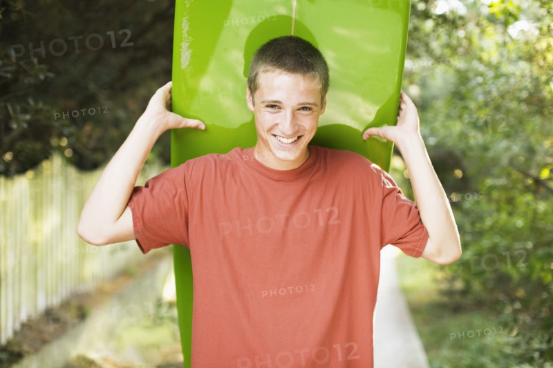 Caucasian teenage boy smiling and holding surfboard