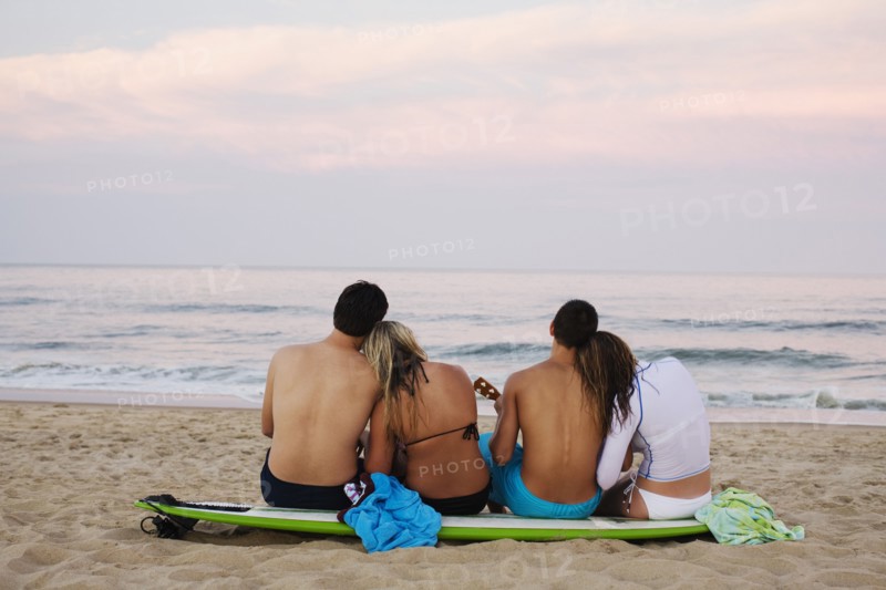 Teenage couples sitting on surfboard on beach