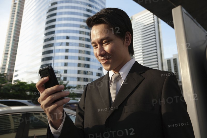 Asian businessman text messaging on cell phone outdoors