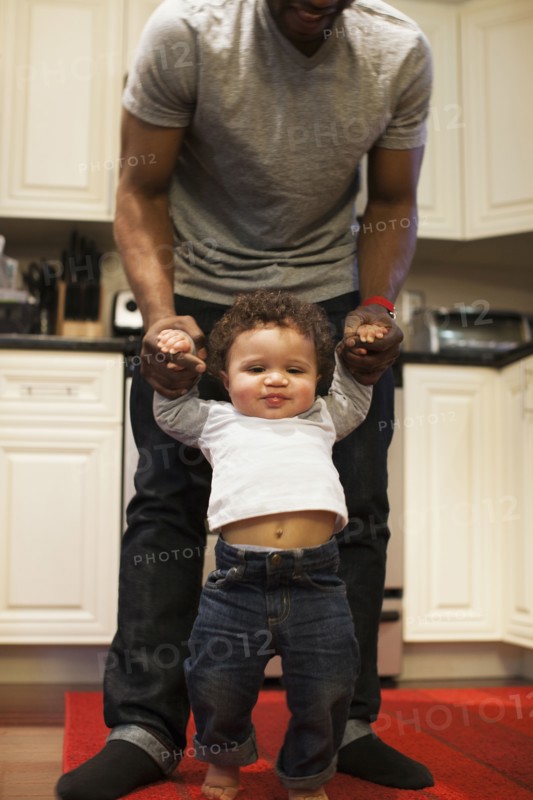 Father helping baby walk in kitchen