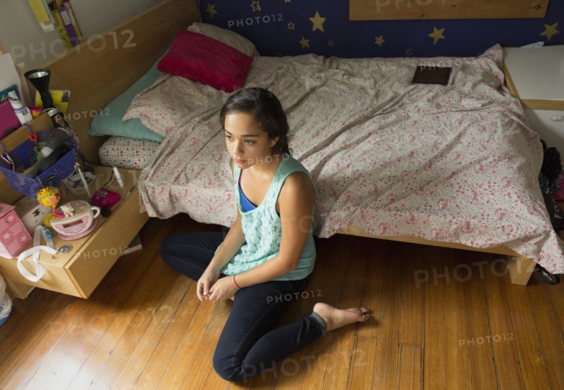 Mixed race girl sitting on bedroom floor