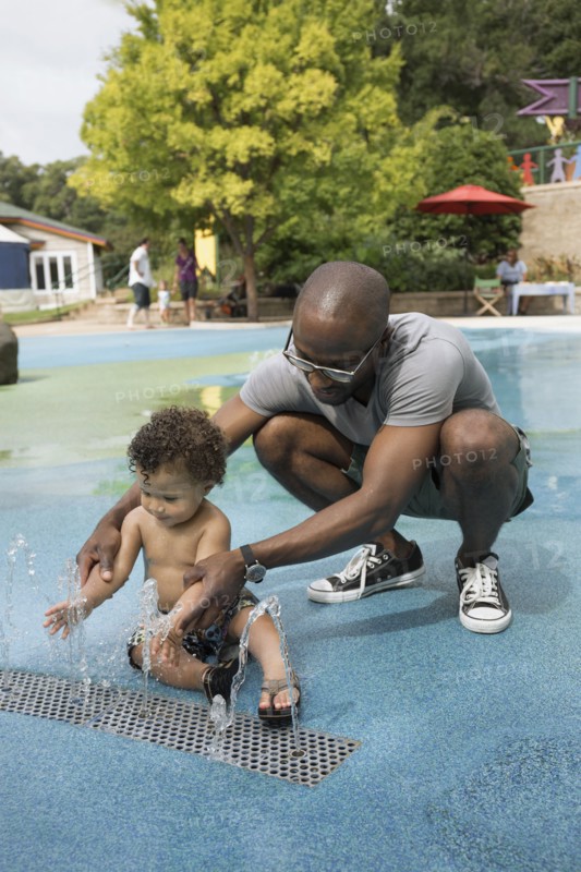Father and toddler son playing in fountain