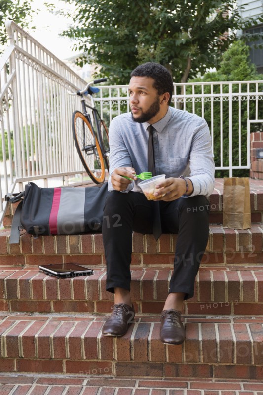 Mixed race businessman eating on front stoop