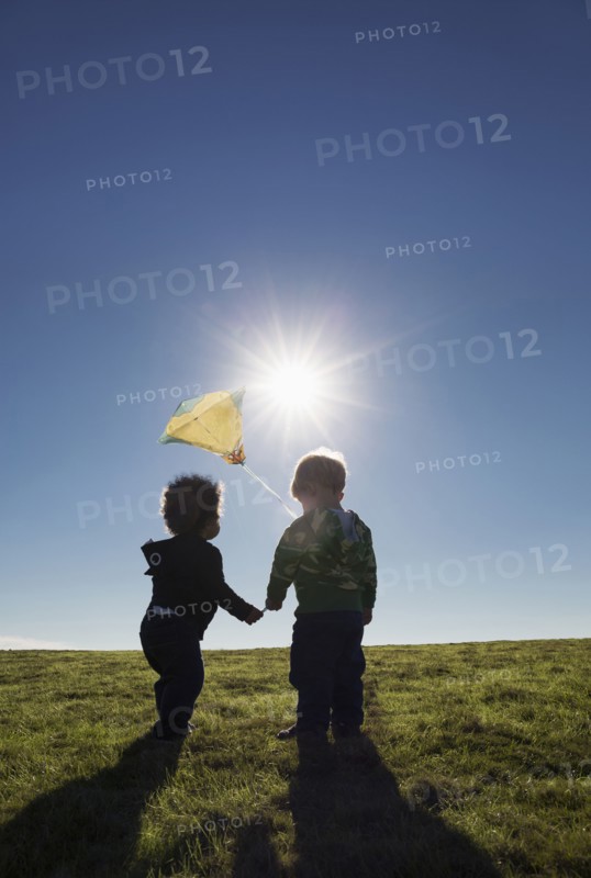Boys watching kite flying against blue sky