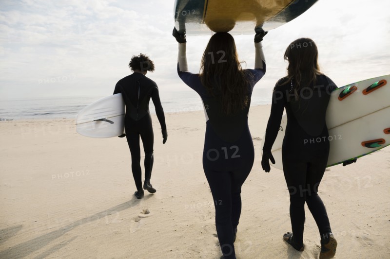 Surfers carrying boards on beach