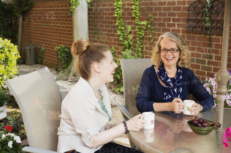 Caucasian mother and daughter drinking coffee in backyard