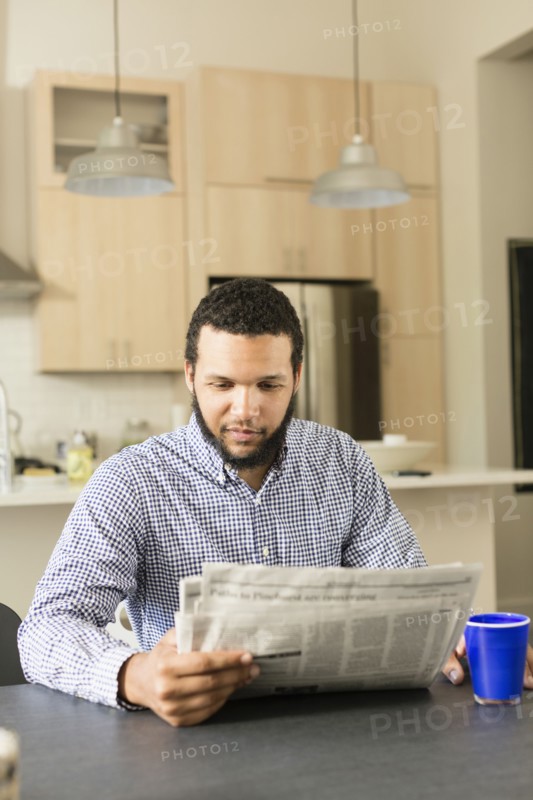 Mixed race man reading newspaper at breakfast table