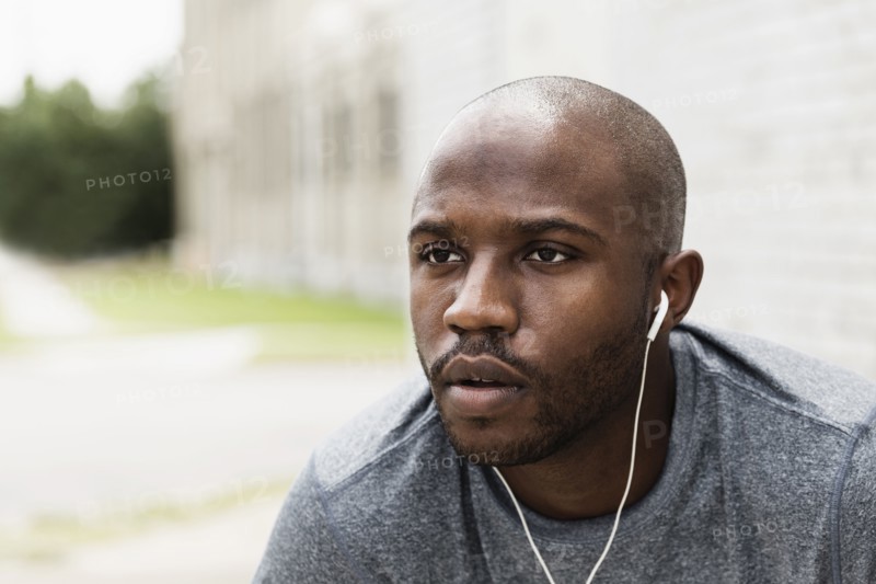 Black runner resting in city with earbuds