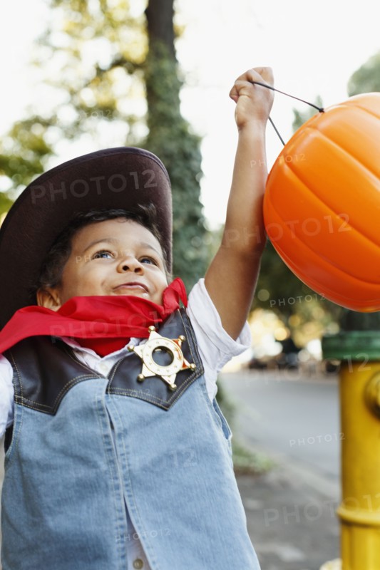 Mixed race boy dressed as cowboy holding pumpkin pail for Halloween