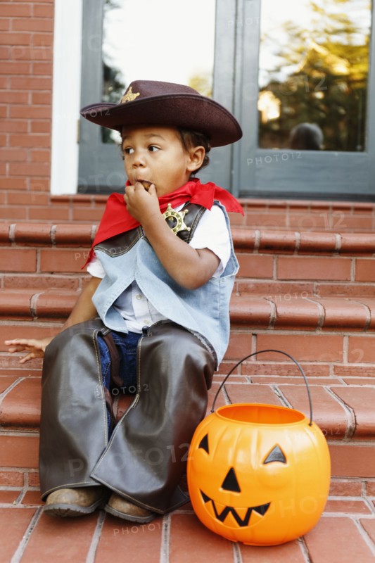 Mixed race boy dressed as cowboy eating Halloween candy