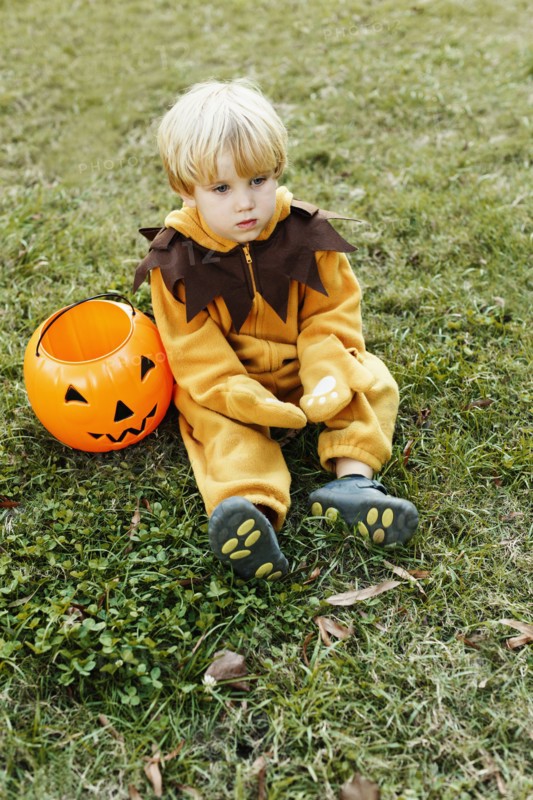 Caucasian boy in lion costume sitting on grass on Halloween