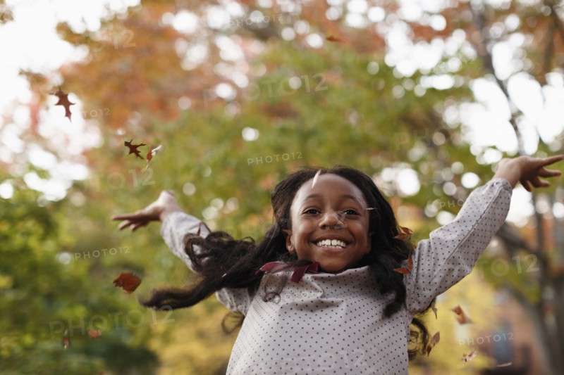 Low angle view of African American girl playing in autumn leaves