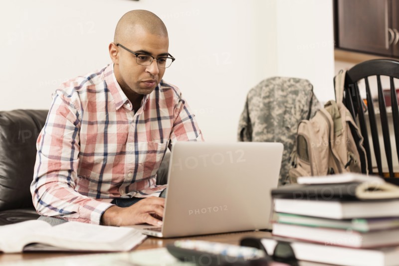 Mixed race soldier using laptop on living room sofa
