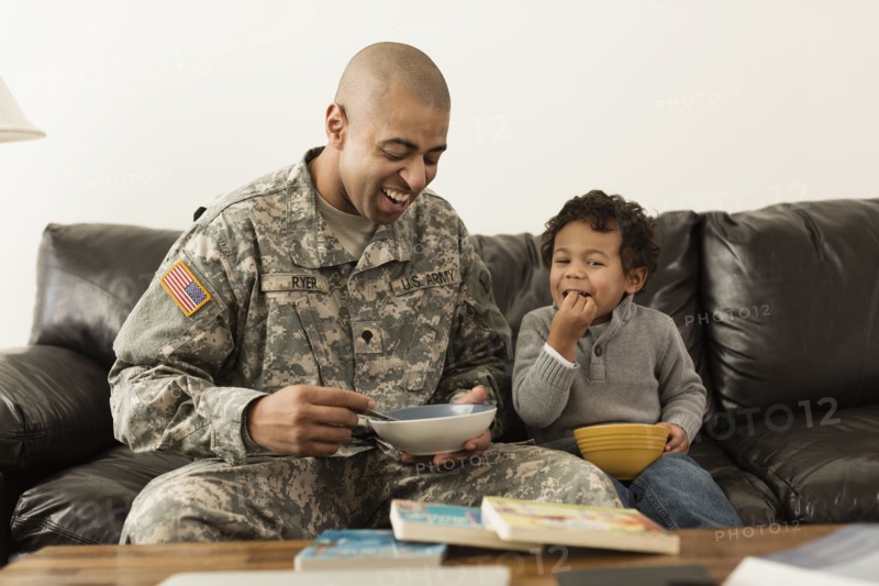 Mixed race soldier father and son from bowls on sofa