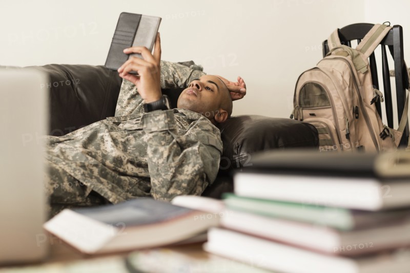Mixed race soldier using digital tablet on sofa near books