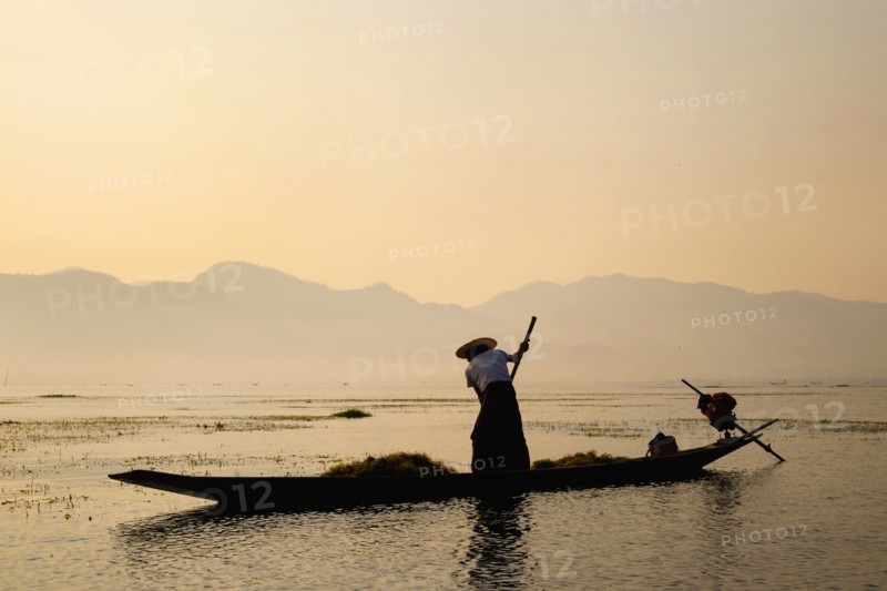 Asian fisherman rowing canoe on rural lake
