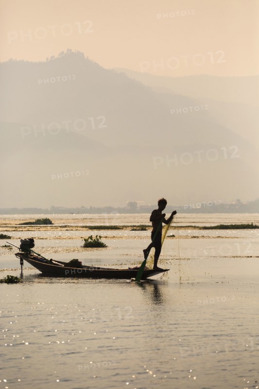 Asian fisherman rowing canoe on rural lake