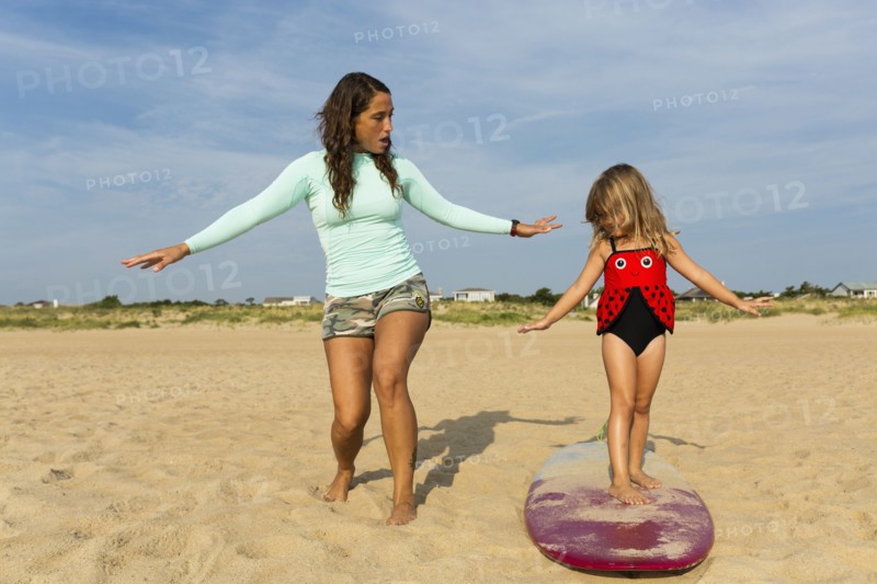 Mother teaching daughter to surf at beach